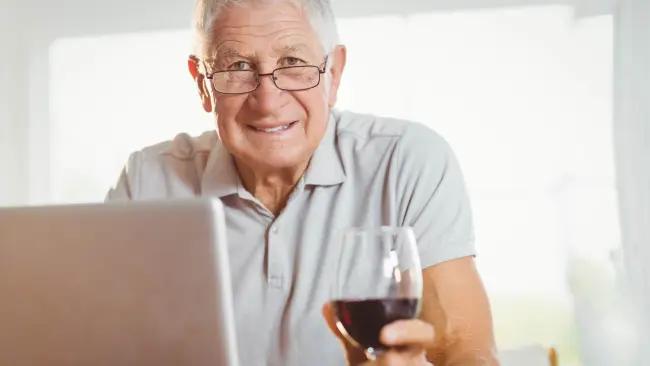 vinprovning - en öldre man med vinglas framför datorn