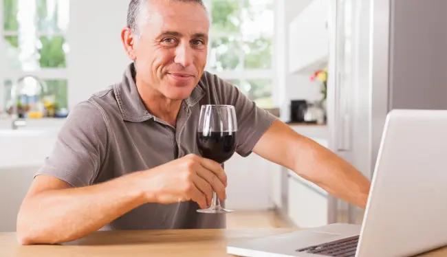 vinprovning - en man skålar med ett glas framför datorn